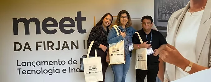 Pessoas com sacolas de evento posam diante de painel com os dizeres Meet da FIRJAN e Lançamento de Tecnologia e Inovação