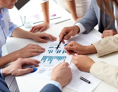Mãos de várias pessoas sobre uma mesa apontando gráficos impressos durante reunião