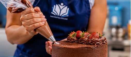 Bolo de chocolate sendo decorado com chantili e morangos