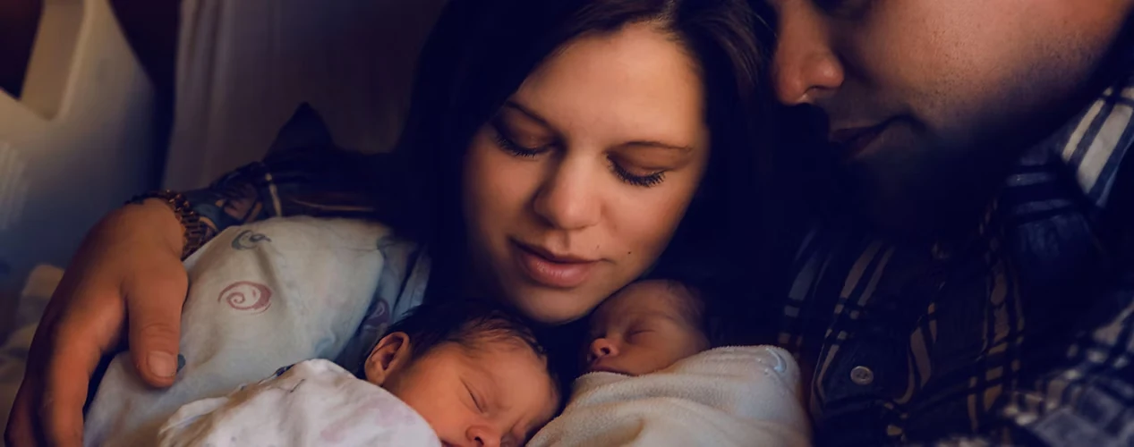 Mãe e pai abraçados aos dois bebês recém-nascidos